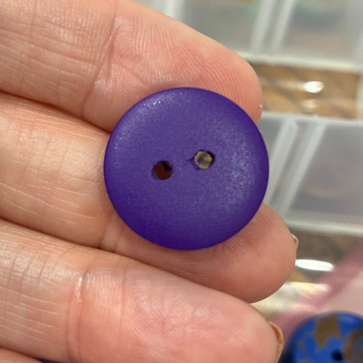 Purple button held between fingers with a container of buttons in the background