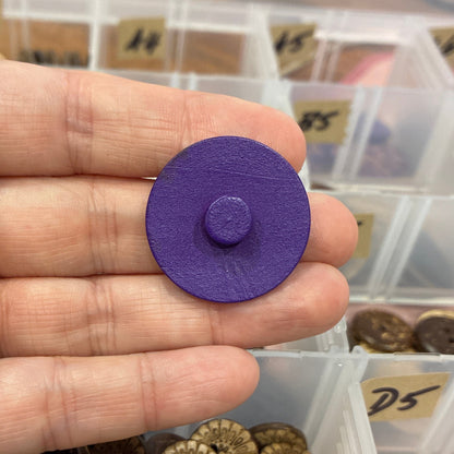 Purple button held in a hand with a container of gold buttons in the background