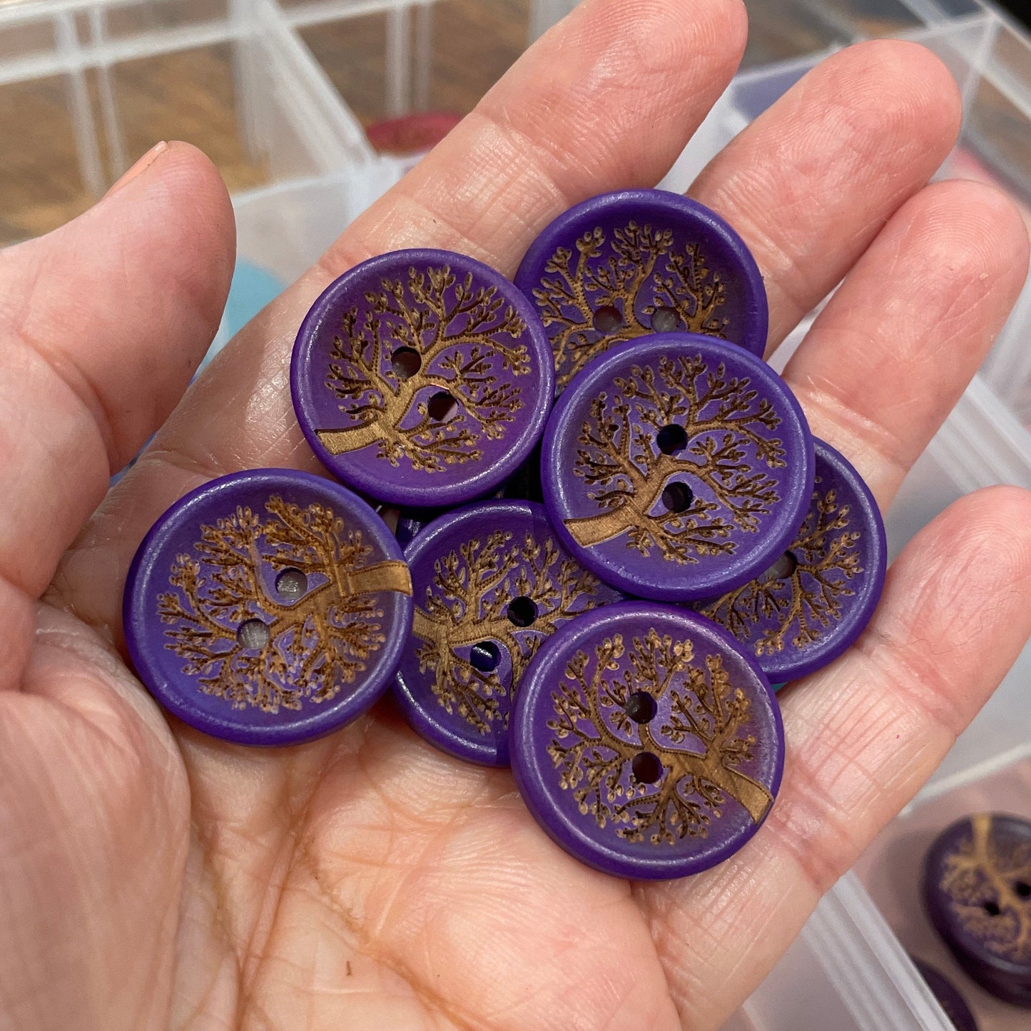 Hand holding purple buttons with intricate designs, with a clear container in the background.