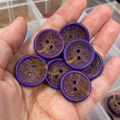 Hand holding purple buttons with intricate designs, with a clear container in the background.