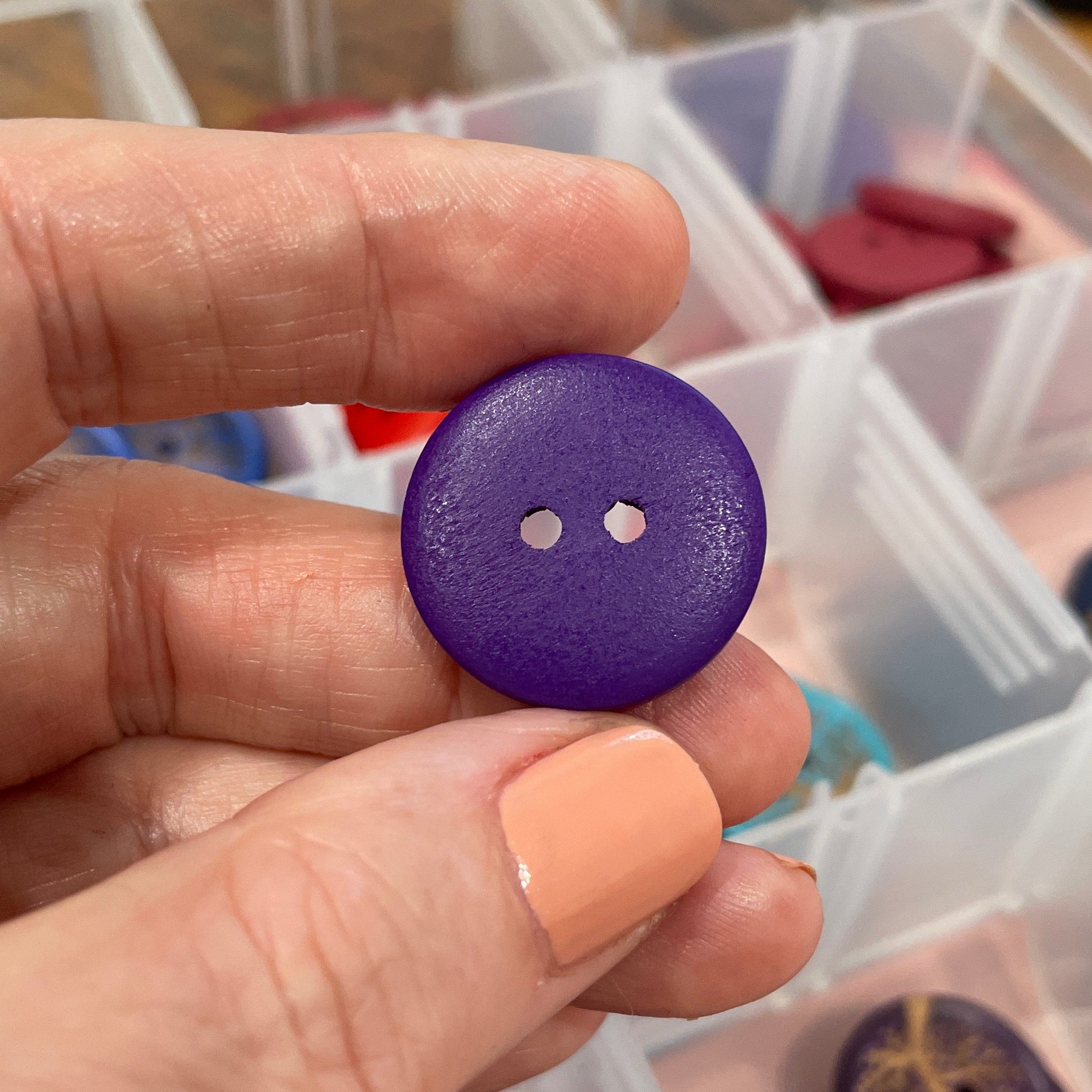Hand holding a purple button with a container of buttons in the background