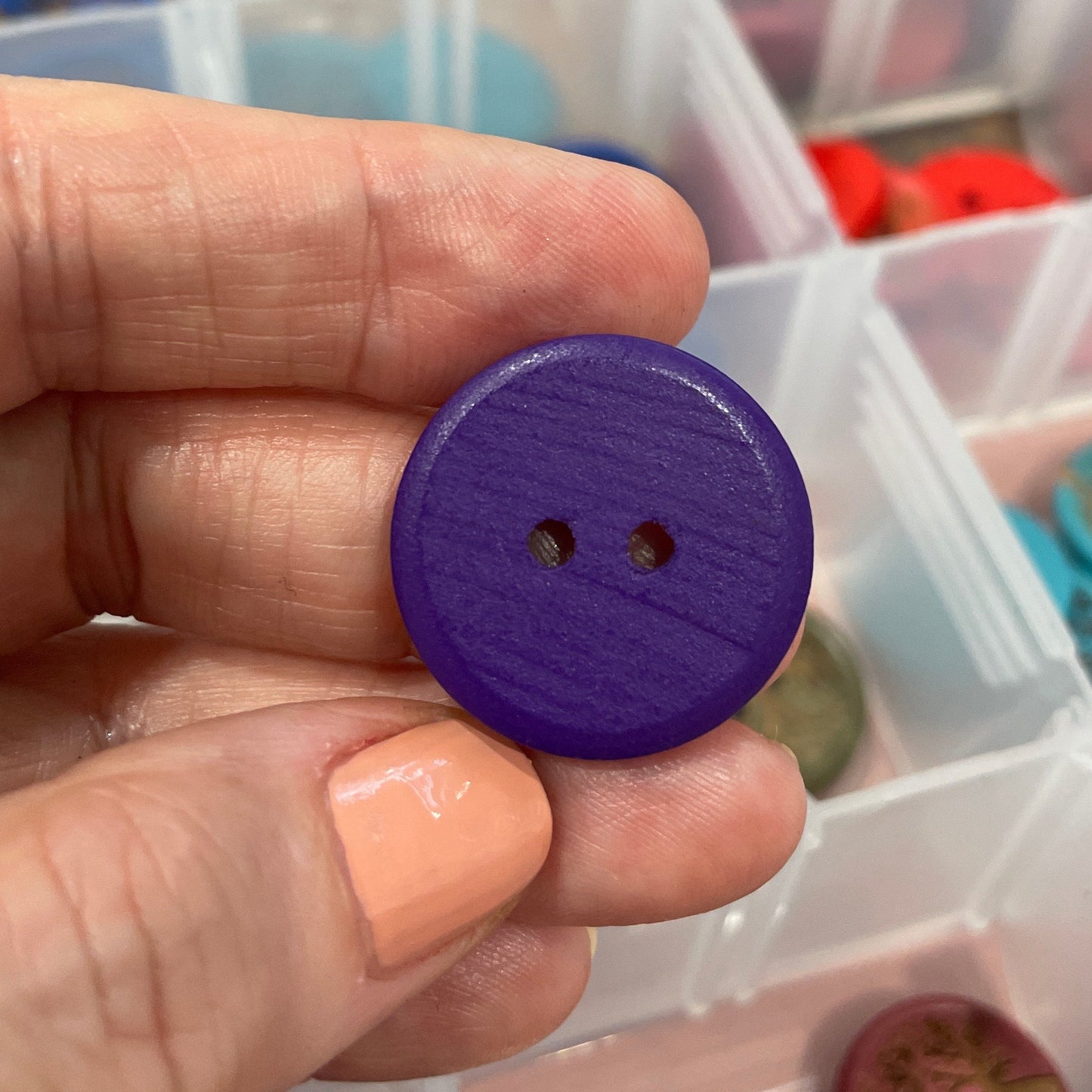 Hand holding a purple button with a container of buttons in the background