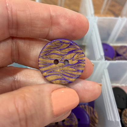 Hand holding a purple and gold button with a container of buttons in the background