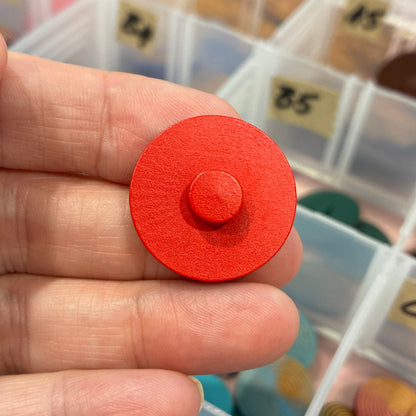 Red button held by a hand with a background of colorful buttons in a case.