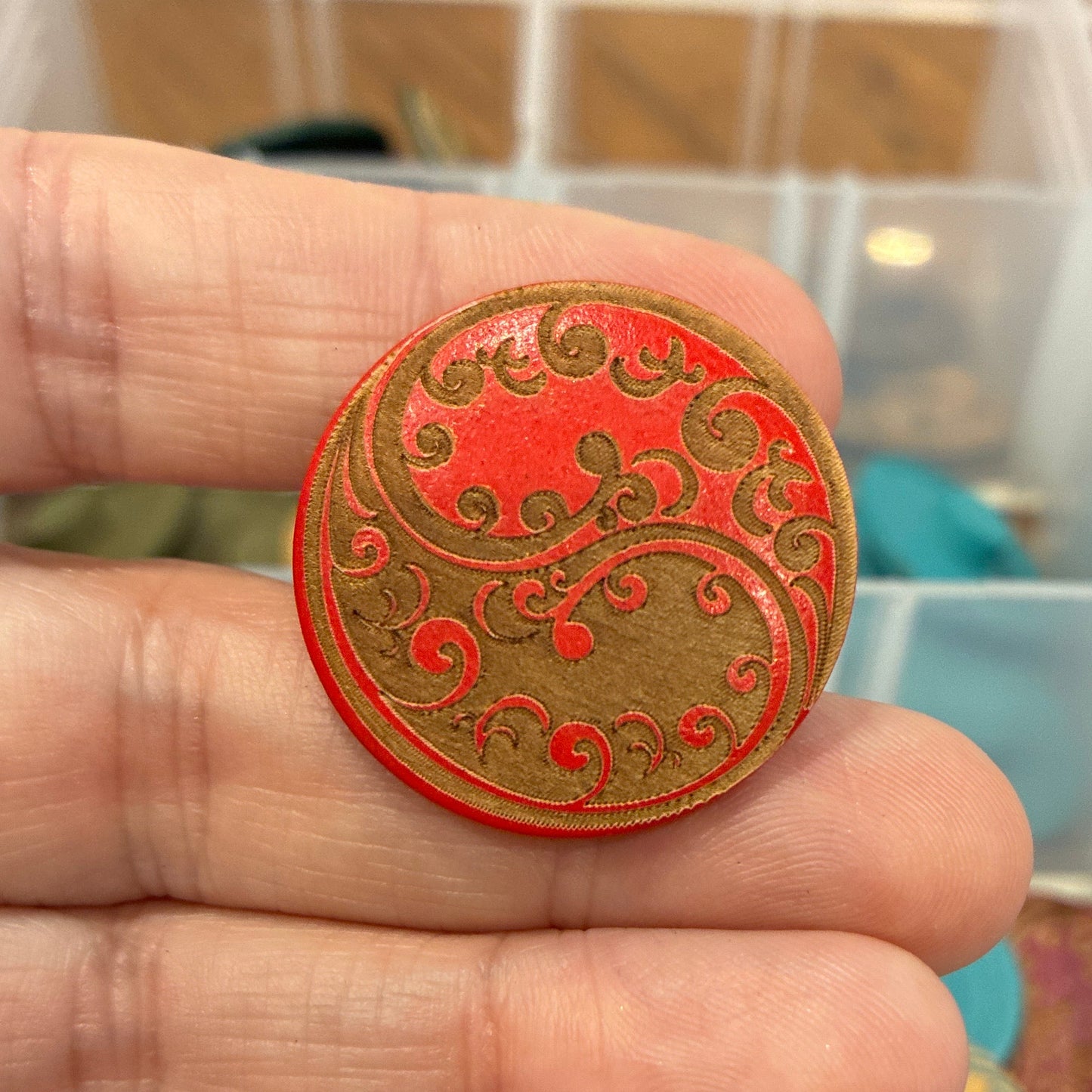 Hand holding a decorative button with a colorful background of storage containers.