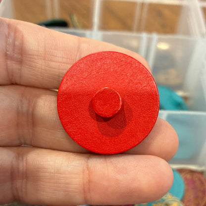 Red circular button held between fingers with a display of colorful circular buttons in the background