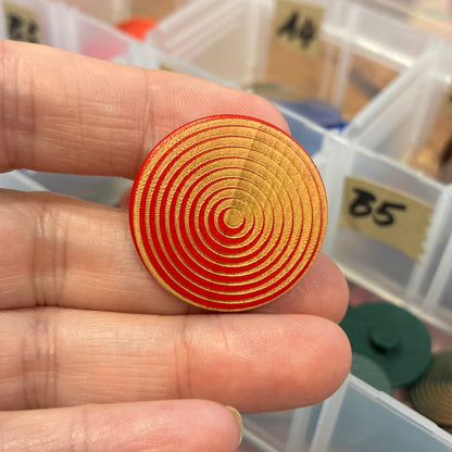 Hand holding a spiral-patterned button with a container of similar objects in the background