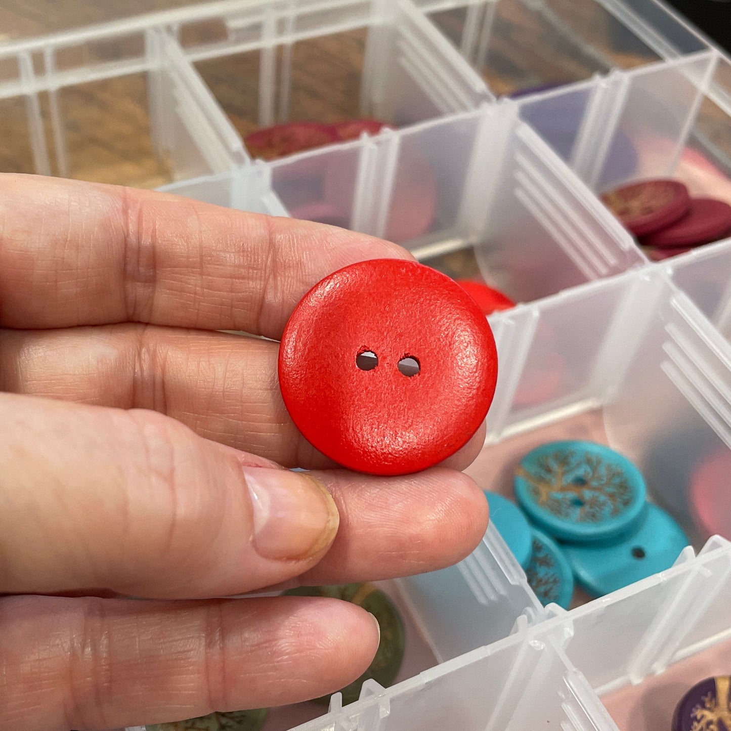 Hand holding a red button with a clear container of assorted buttons in the background