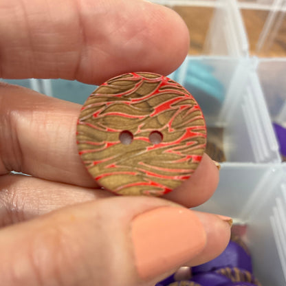 Hand holding a button with a colorful pattern against a background of a button organizer.
