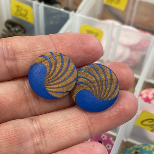 Hand holding two blue buttons with yellow patterns in front of a container of assorted buttons.
