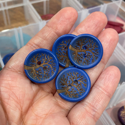 Hand holding blue buttons with tree designs, with a blurred background
