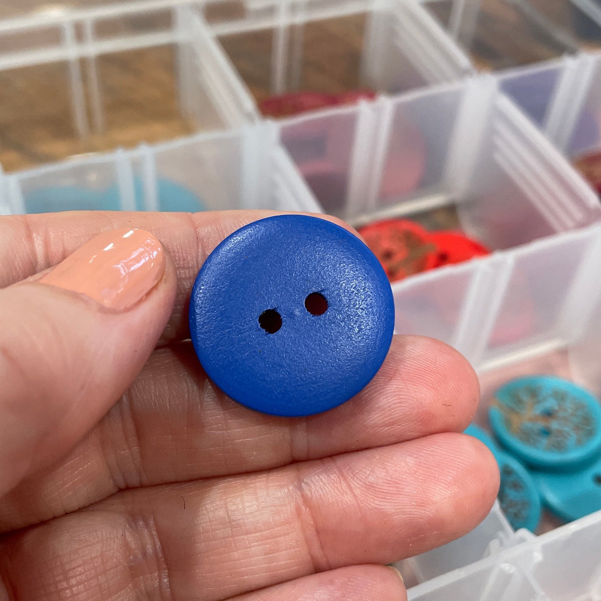 Hand holding a blue button with a clear container of buttons in the background