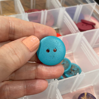 Hand holding a blue button with a container of buttons in the background