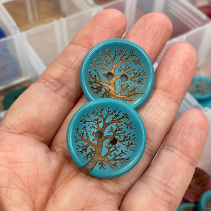 Hand holding two blue buttons with tree design in front of a clear box.