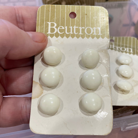 Hand holding a small cardboard packaging with white buttons, branded 'Beutron'.