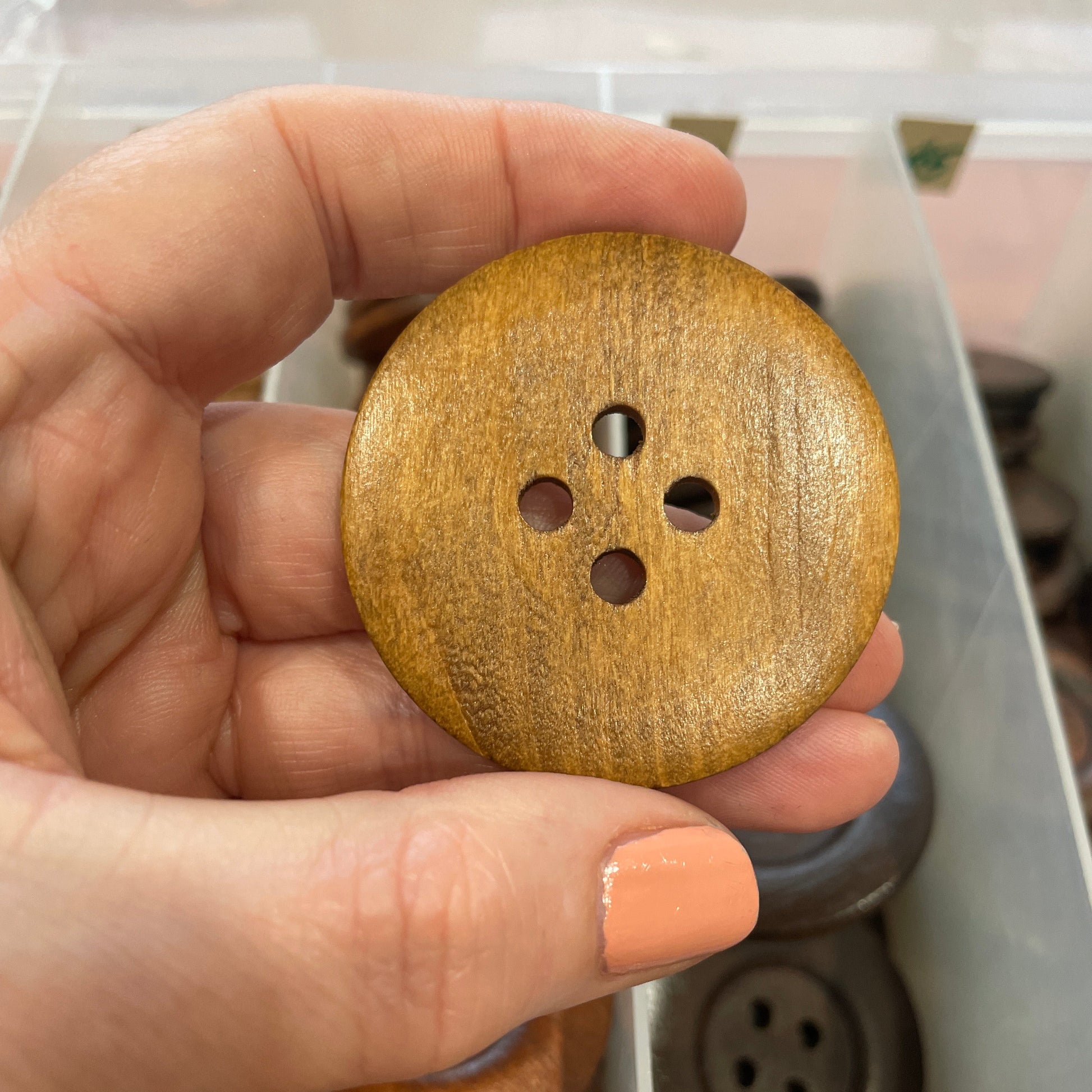 Hand holding a wooden button with a blurred background of a button collection.