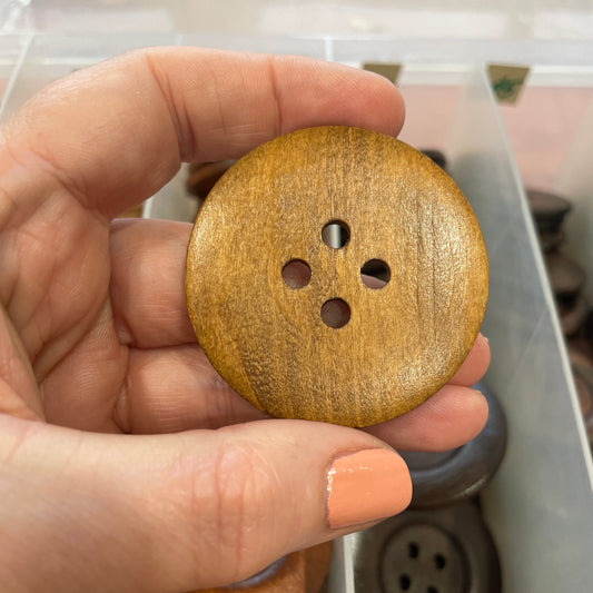 Hand holding a wooden button with a blurred background of a button collection.