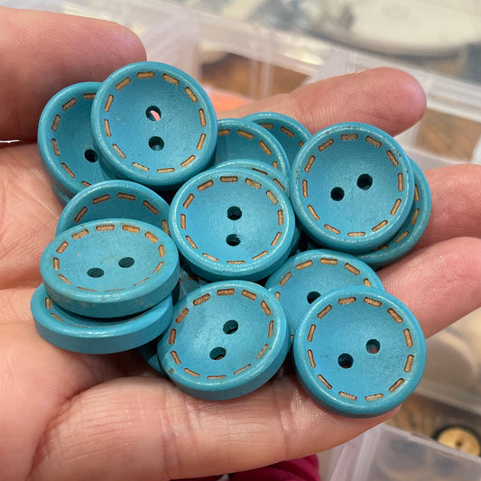 Hand holding blue buttons with a container of orange and pink buttons in the background.
