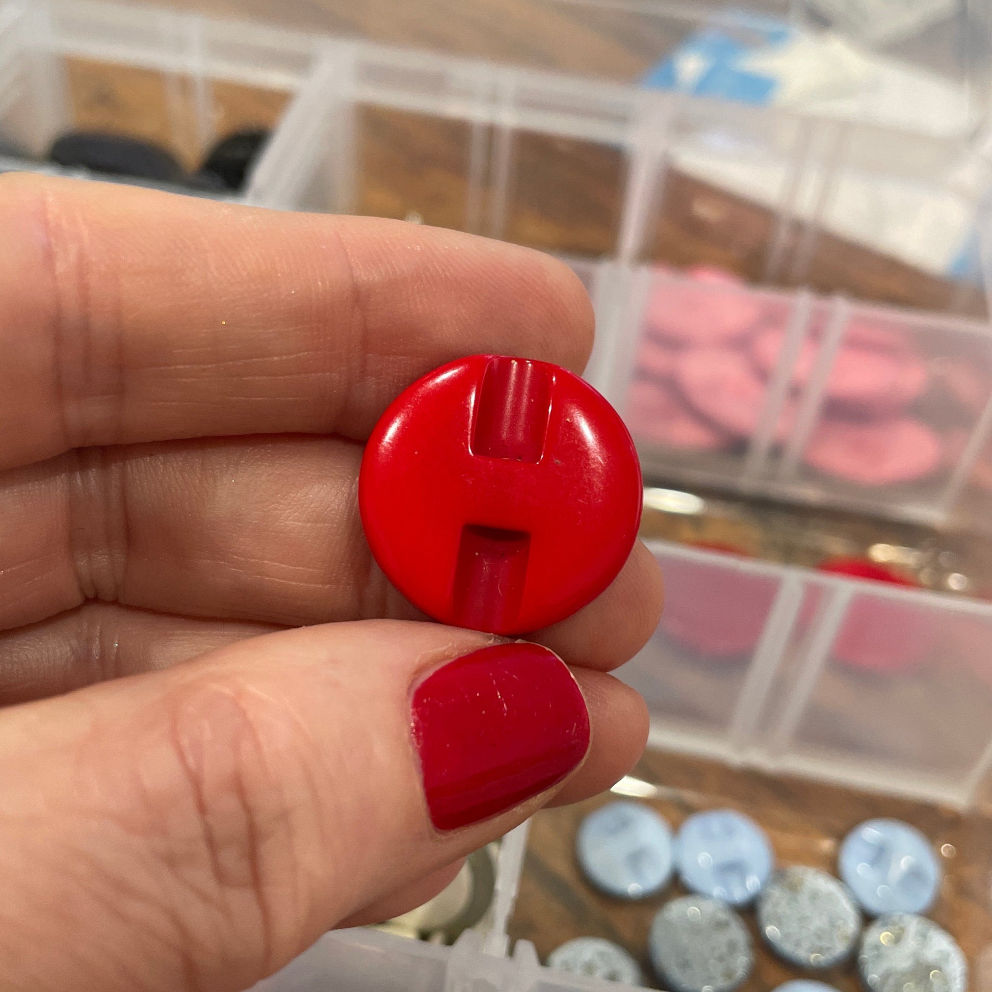 Hand holding a red button with a container of buttons in the background