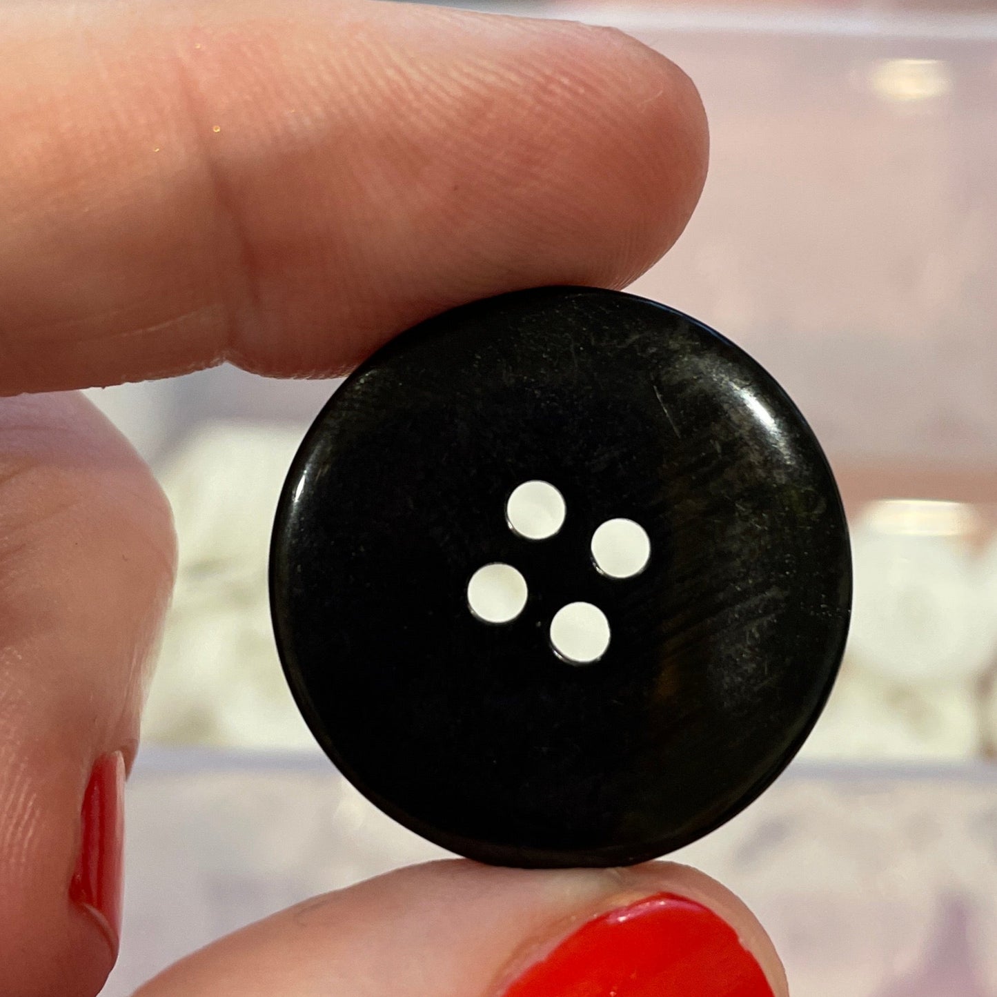 Black button held between fingers with a container of buttons in the background