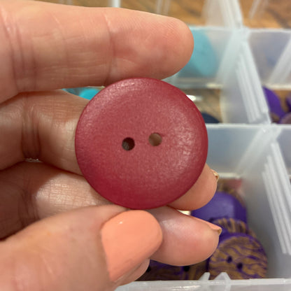 Hand holding a pink button with a blurred background of a storage container with various items.