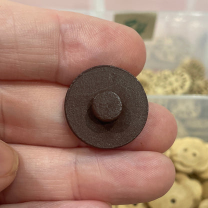 Hand holding a brown button with a collection of buttons in the background