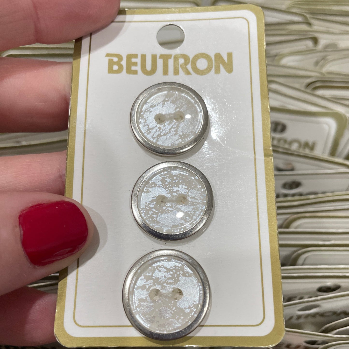 Three buttons on a Beutron card held by a hand with red nail polish.