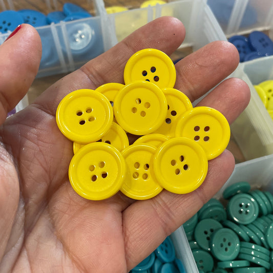 Hand holding yellow buttons with a container of assorted colored buttons in the background
