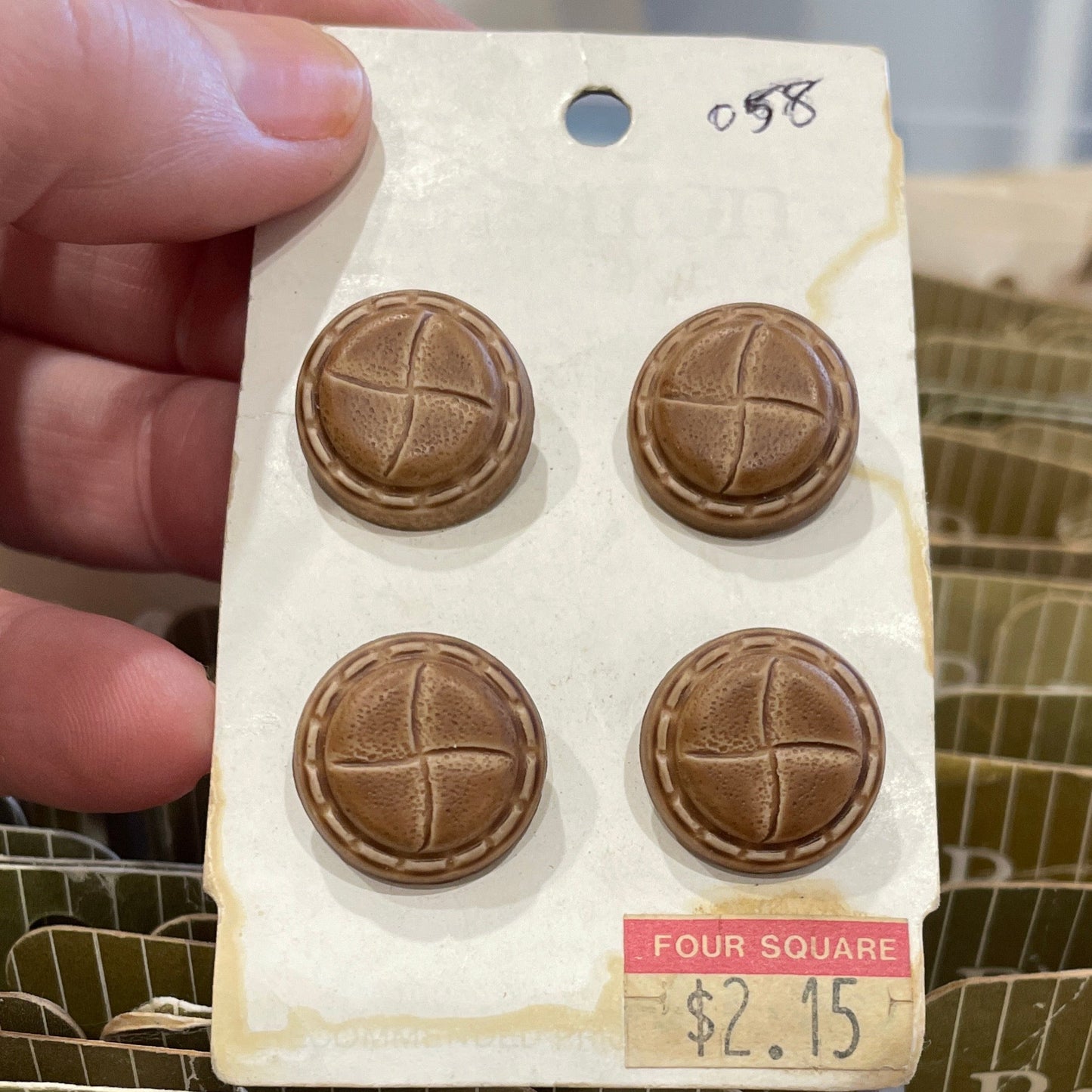 Four brown buttons on a card held by a hand with a blurred background