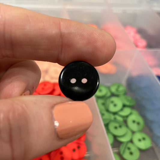 Black button held between fingers with colorful buttons in a container in the background