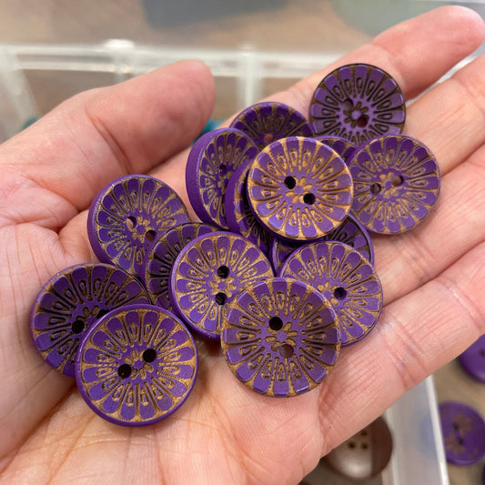 Hand holding purple buttons with gold patterns, blurred background