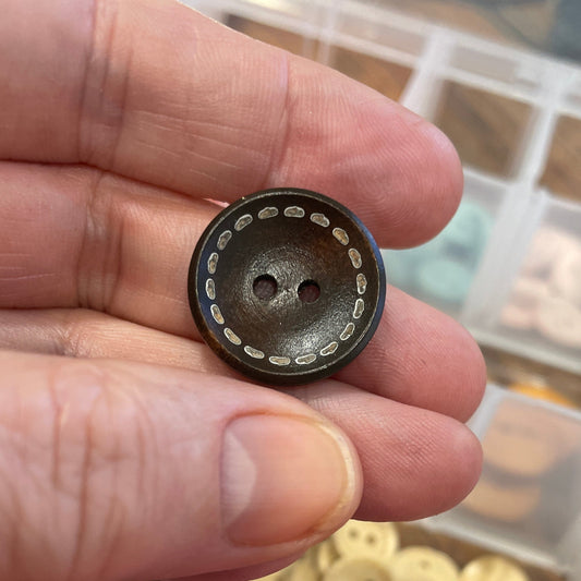 Hand holding a black button with a container of colorful buttons in the background