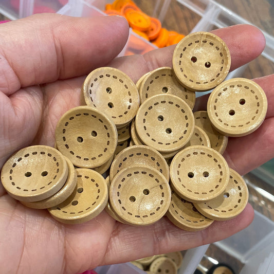 Hand holding a collection of wooden buttons with a container of assorted buttons in the background.