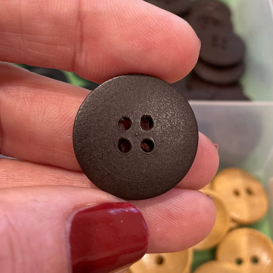 Hand holding a brown button with a container of various buttons in the background