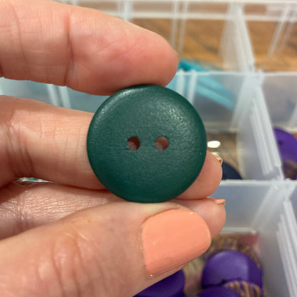 Hand holding a green button with a container of buttons in the background
