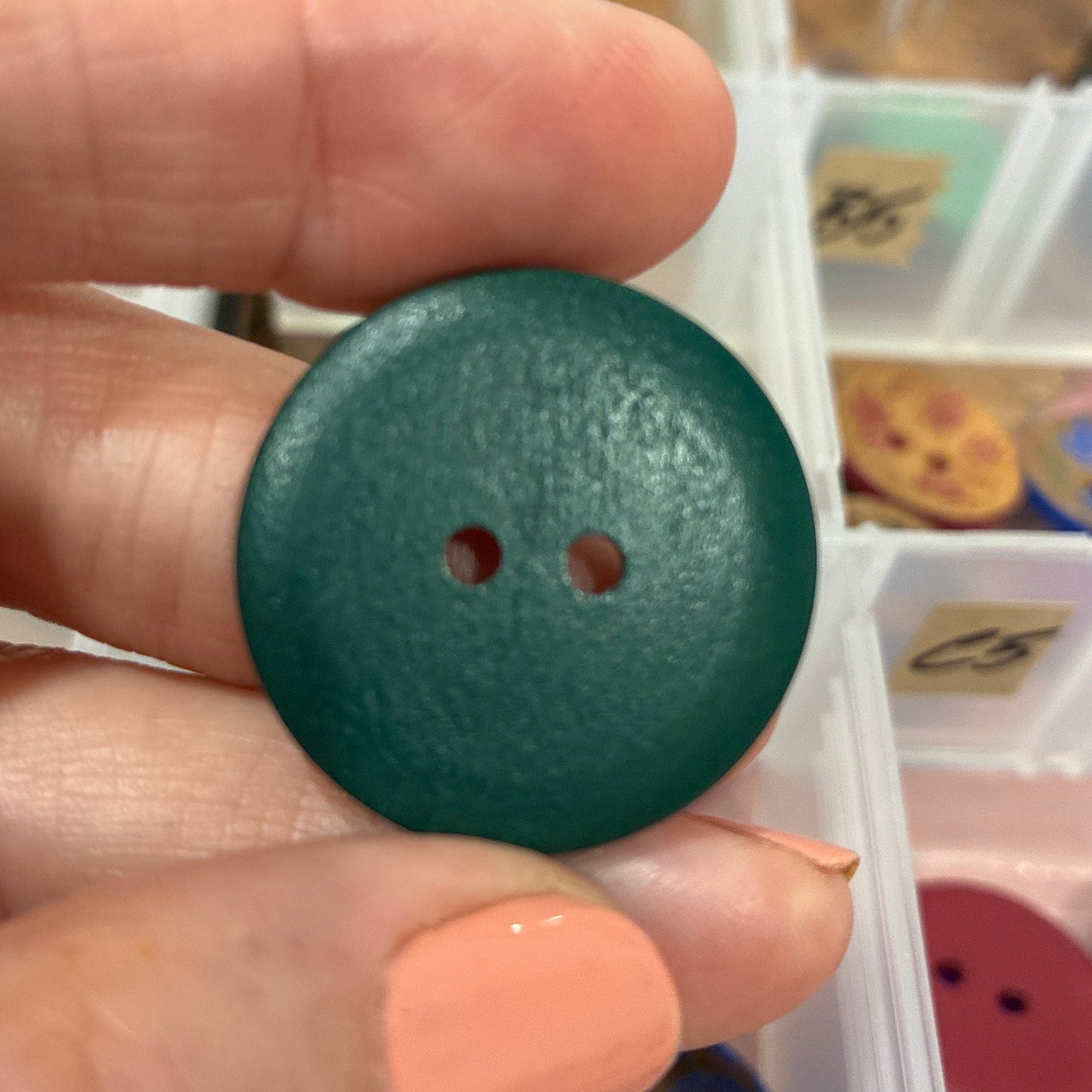 Green button held between fingers with a container of buttons in the background