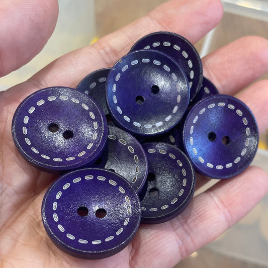 Hand holding purple buttons with white stitching against a blurred background