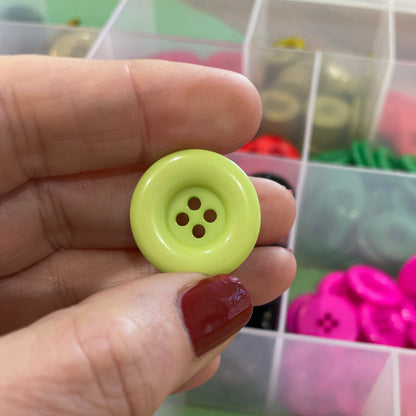 Hand holding a green button with a container of assorted buttons in the background