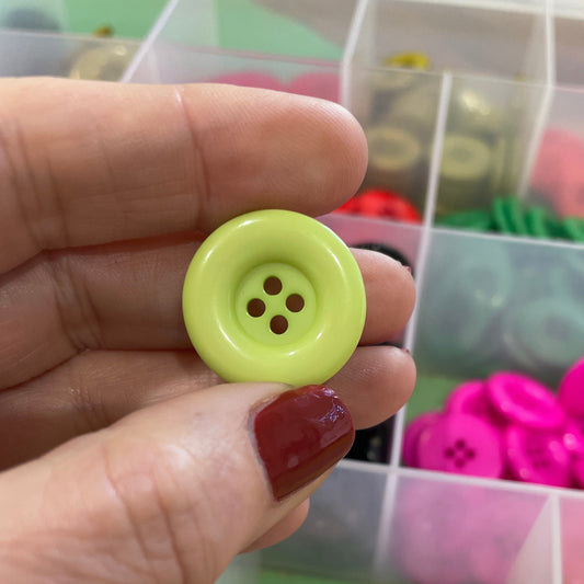 Hand holding a green button with a container of assorted buttons in the background