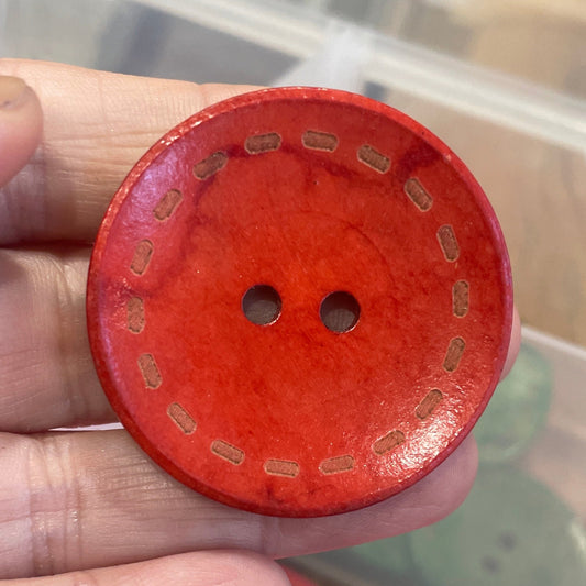 Red button held by a hand with a container of buttons in the background