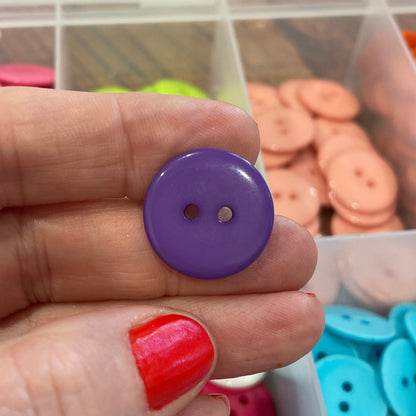 Hand holding a purple button with containers of colorful buttons in the background