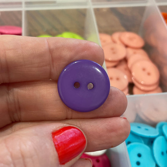 Hand holding a purple button with containers of colorful buttons in the background