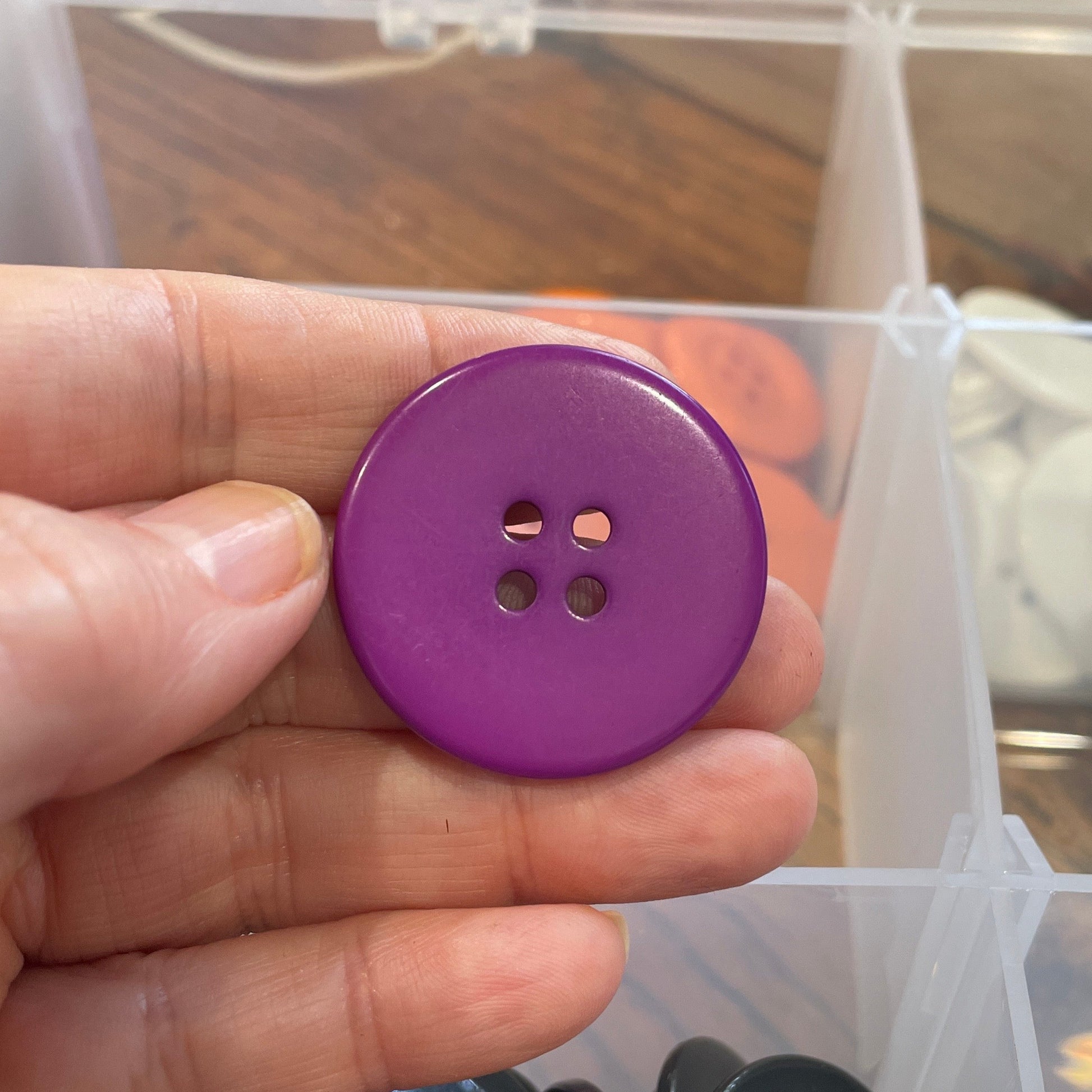 Purple button held in hand with clear container of buttons in background