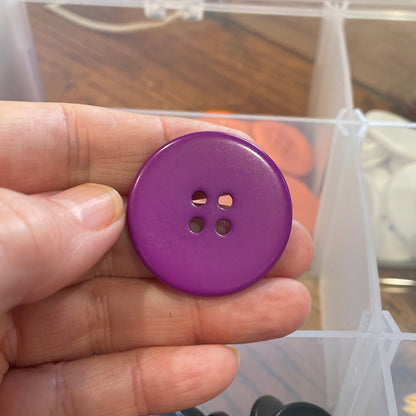 Purple button held in hand with clear container of buttons in background