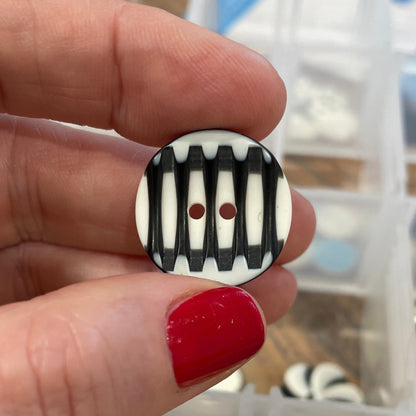 Hand holding a black and white striped button with a container of buttons in the background