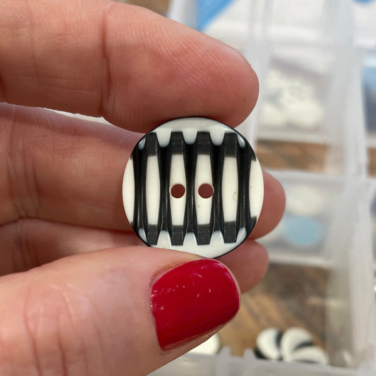 Hand holding a black and white striped button with a container of buttons in the background