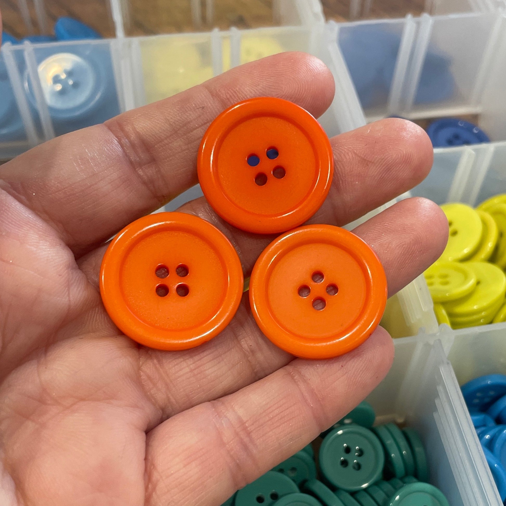 Hand holding orange buttons with a container of colorful buttons in the background