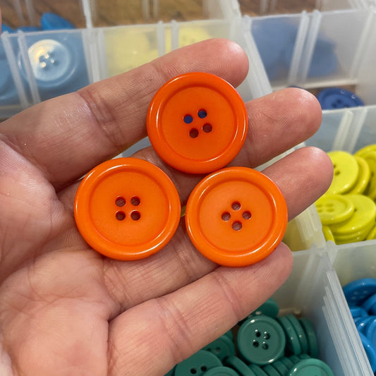 Hand holding orange buttons with a container of colorful buttons in the background