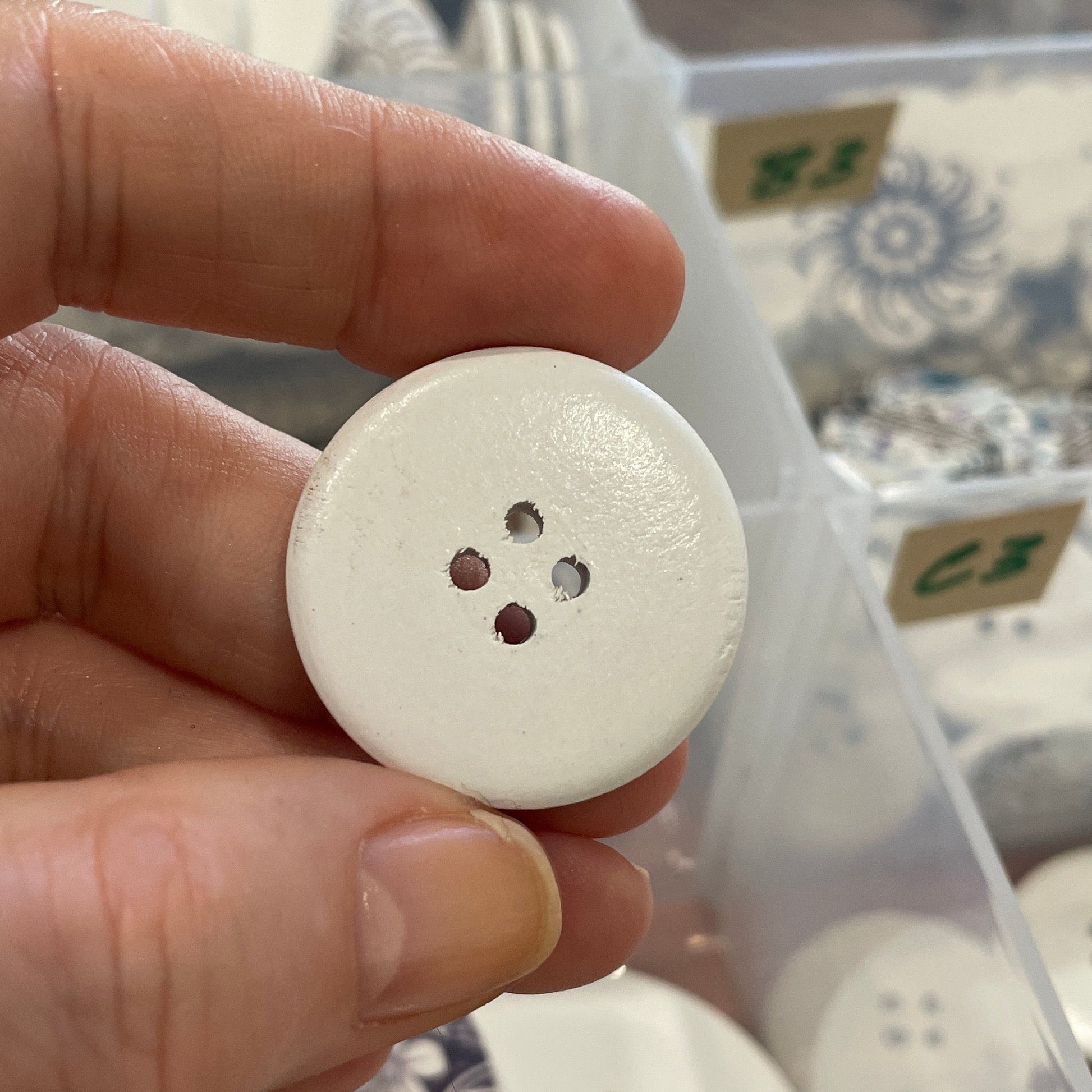 Hand holding a white button with a clear container of buttons in the background