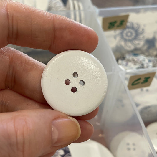 Hand holding a white button with a clear container of buttons in the background